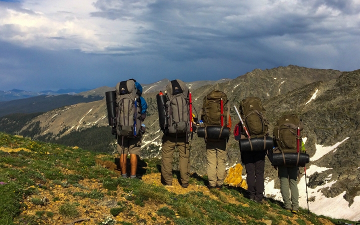 Five people with backpacks overlook a mountainous landscape